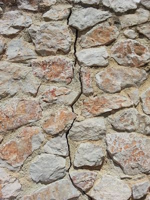 A section of an old stone wall, with a crack zig-zagging between the unevenly-shaped rocks